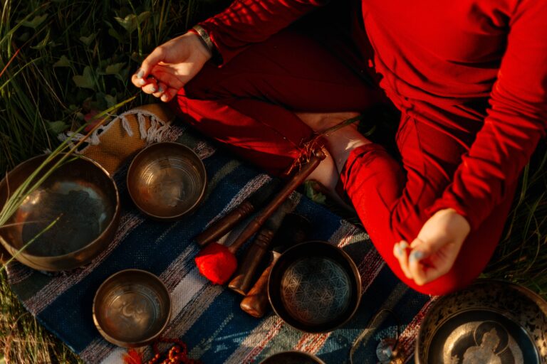 Close-up of singing bowls and mallets beside a person in red clothing.