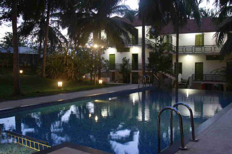 Swimming pool at Anandakosha retreat lit up at night with palm trees
