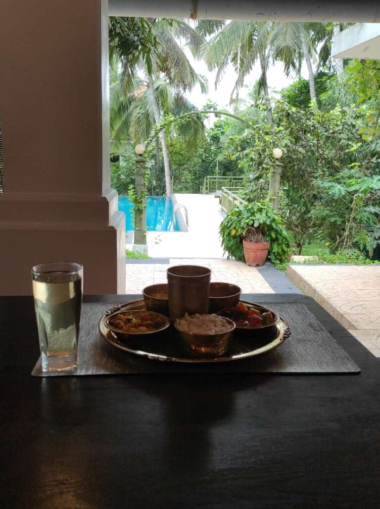 ayurvedic food on table with water and coconut trees near swimming pool at ayurvedic resort in kerela